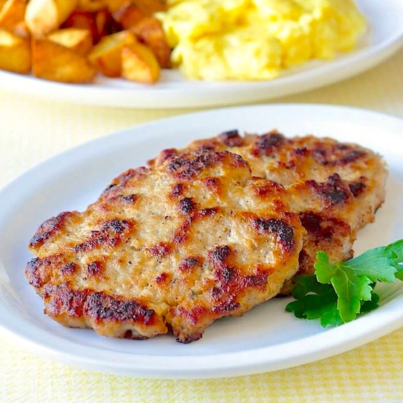 Cooked Cumberland sausage patties on a white plate for Social Media posting