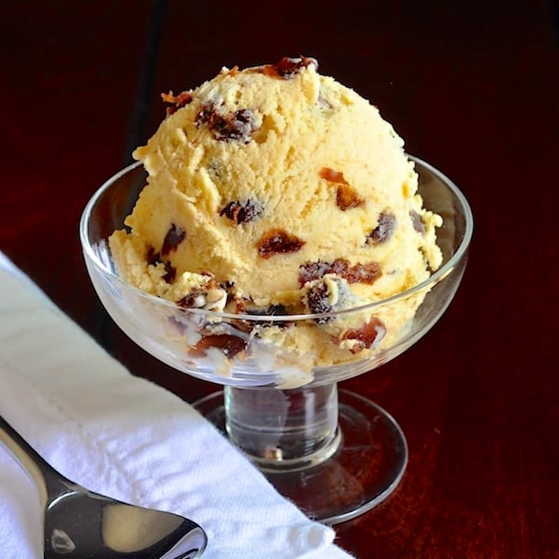 Wide shot photo of one scoop of Rum Raisin Ice Cream in a clear glass dish.