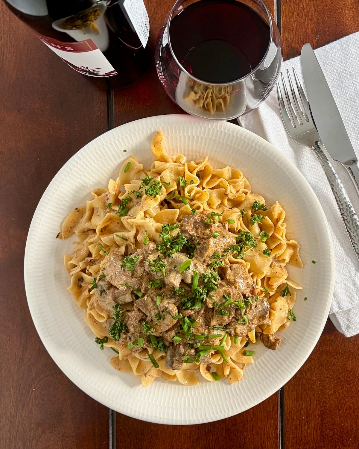 Beef Stroganoff photo of one serving on a white plate with wine and bottle taken from overhead