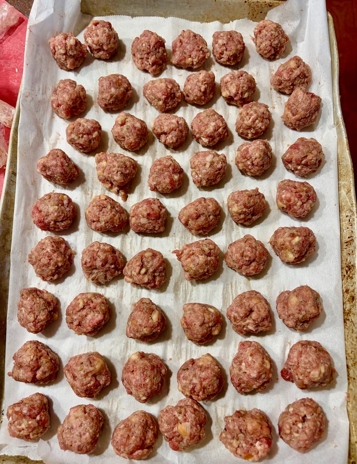 Mini meatballs rolled on a parchment lined baking sheet.