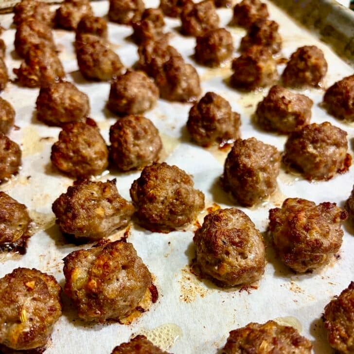 Close up photo of mini meatballs, fully cooked on a baking sheet.