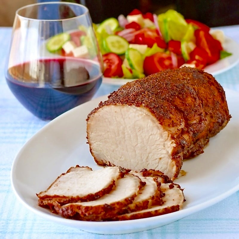 Brined Roast Pork Loin on a white platter with salad and wine in background