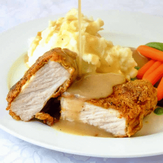 Chicken Fried Pork Chops photo of one serving in a white plate with gravy being poured on