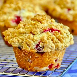 Cranberry Crunch Muffins. single muffin with muffins on cooling rack in background.