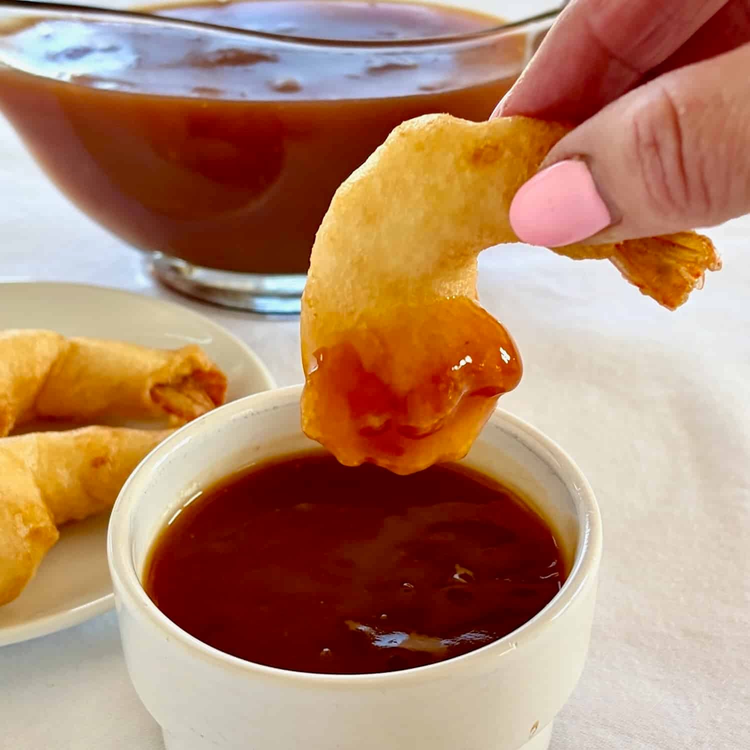 Photo of a single battered shrimp being dipped in sweet and sour sauce.