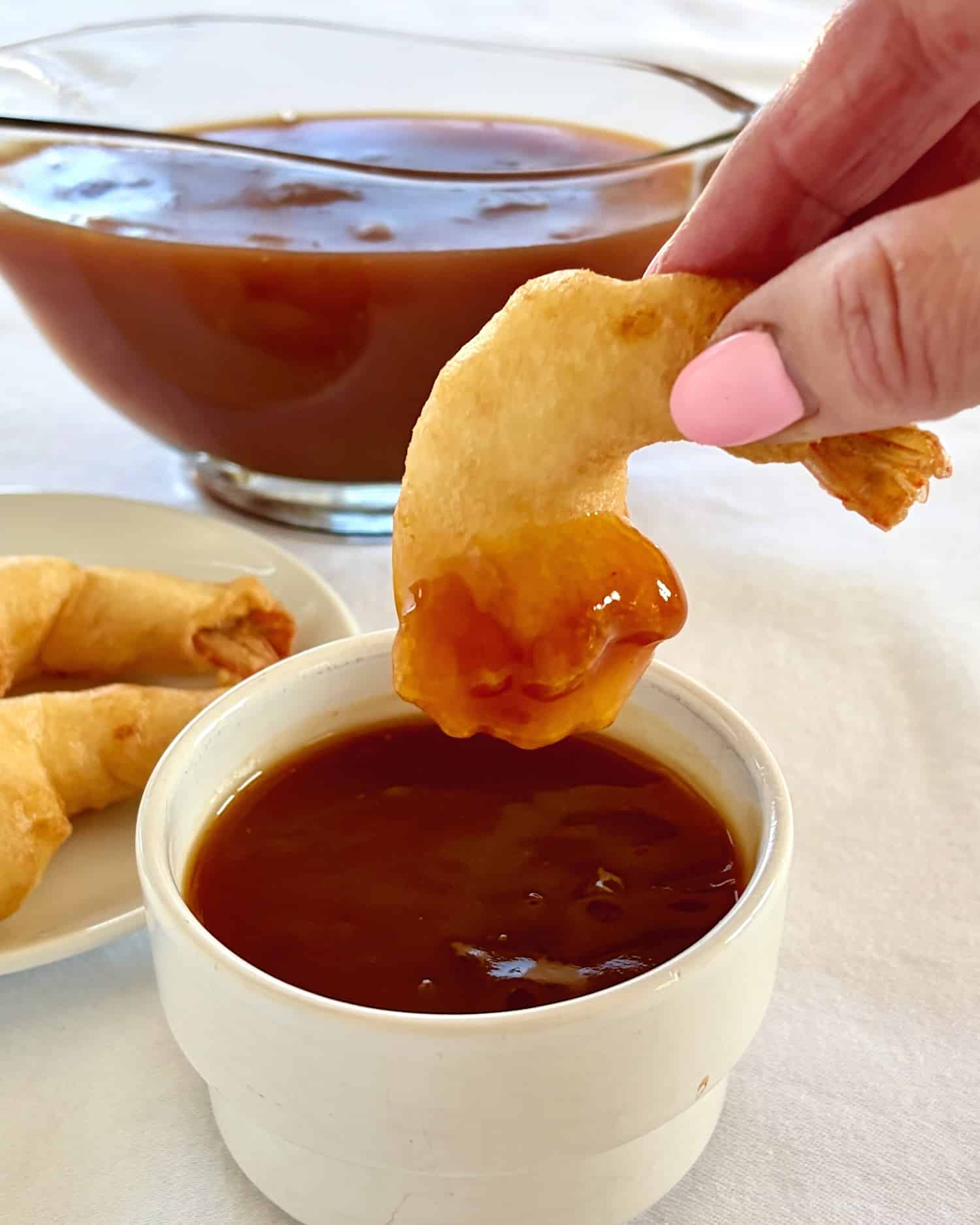 Photo of a battered shrimp being dipped into a ramekin of sweet and sour sauce.