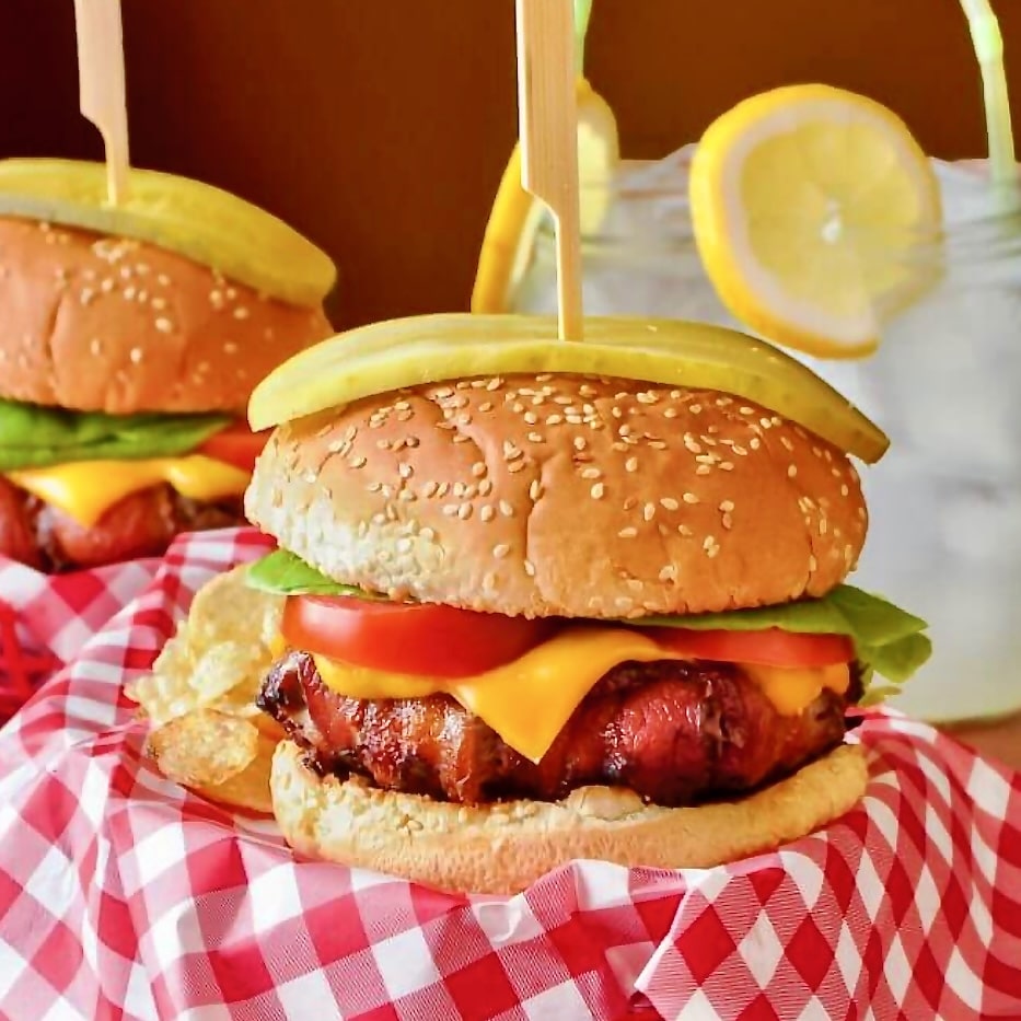 The Ultimate Bacon Wrapped Cheeseburger pictured in a takeout basket with lemonade in the background