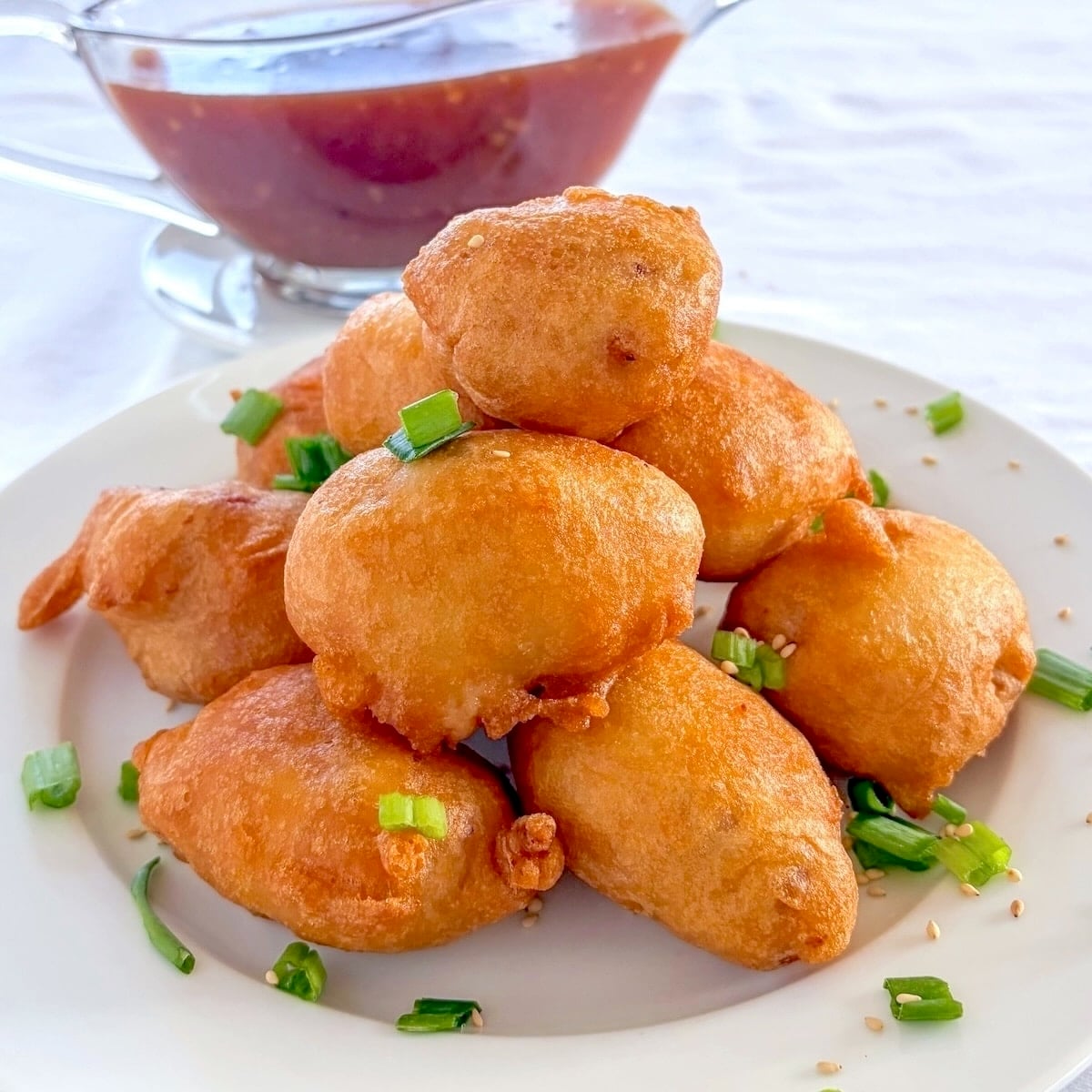 Chinese Chicken Balls photo with balls stacked on a plate with sweet and sour sauce in the background.