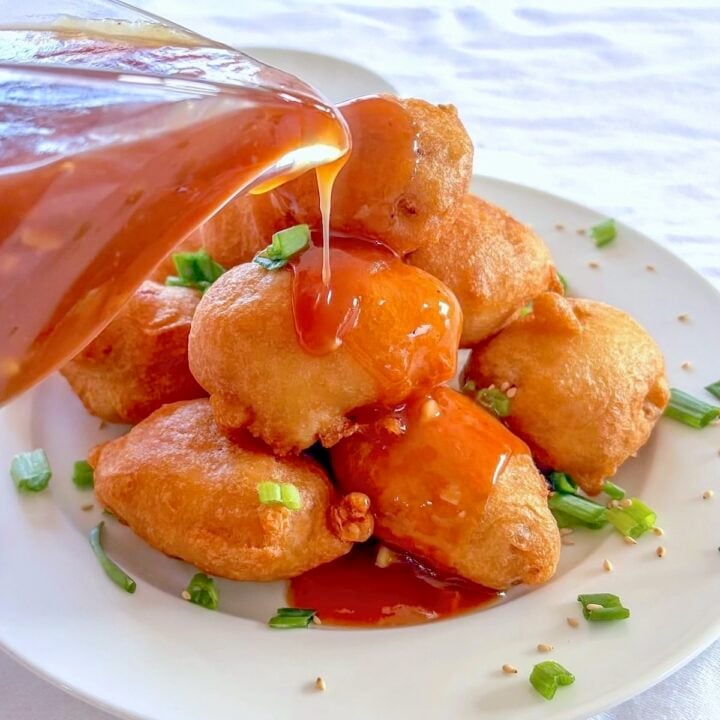 Chinese Chicken Balls photo with balls stacked on a plate with sweet and sour sauce being pored over the top.