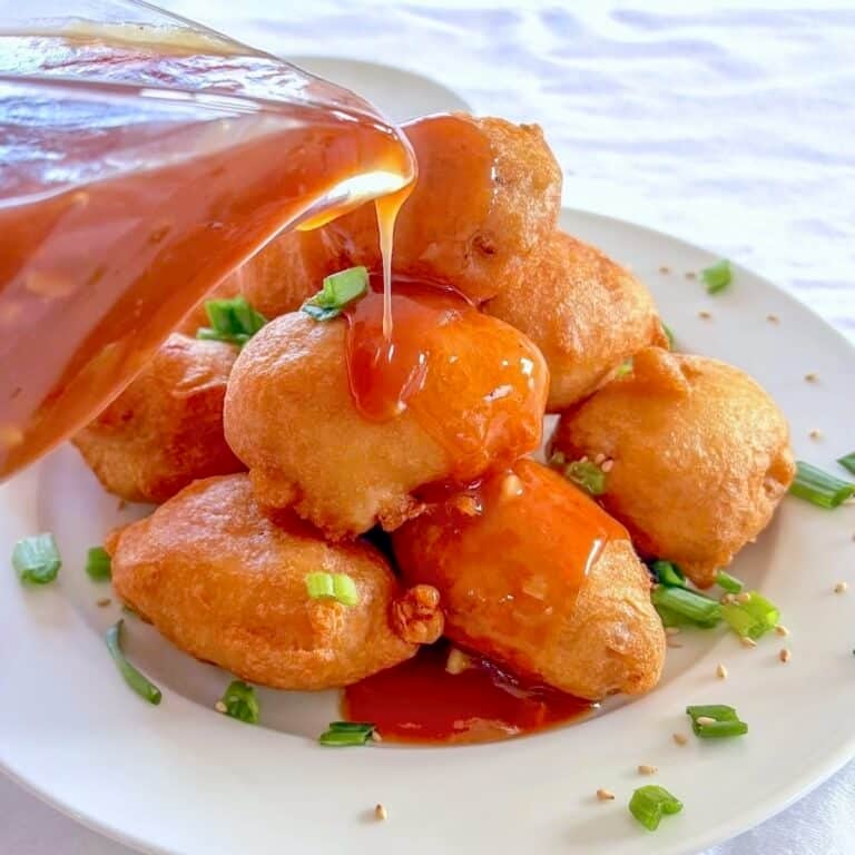 Chinese Chicken Balls photo with balls stacked on a plate with sweet and sour sauce being pored over the top.