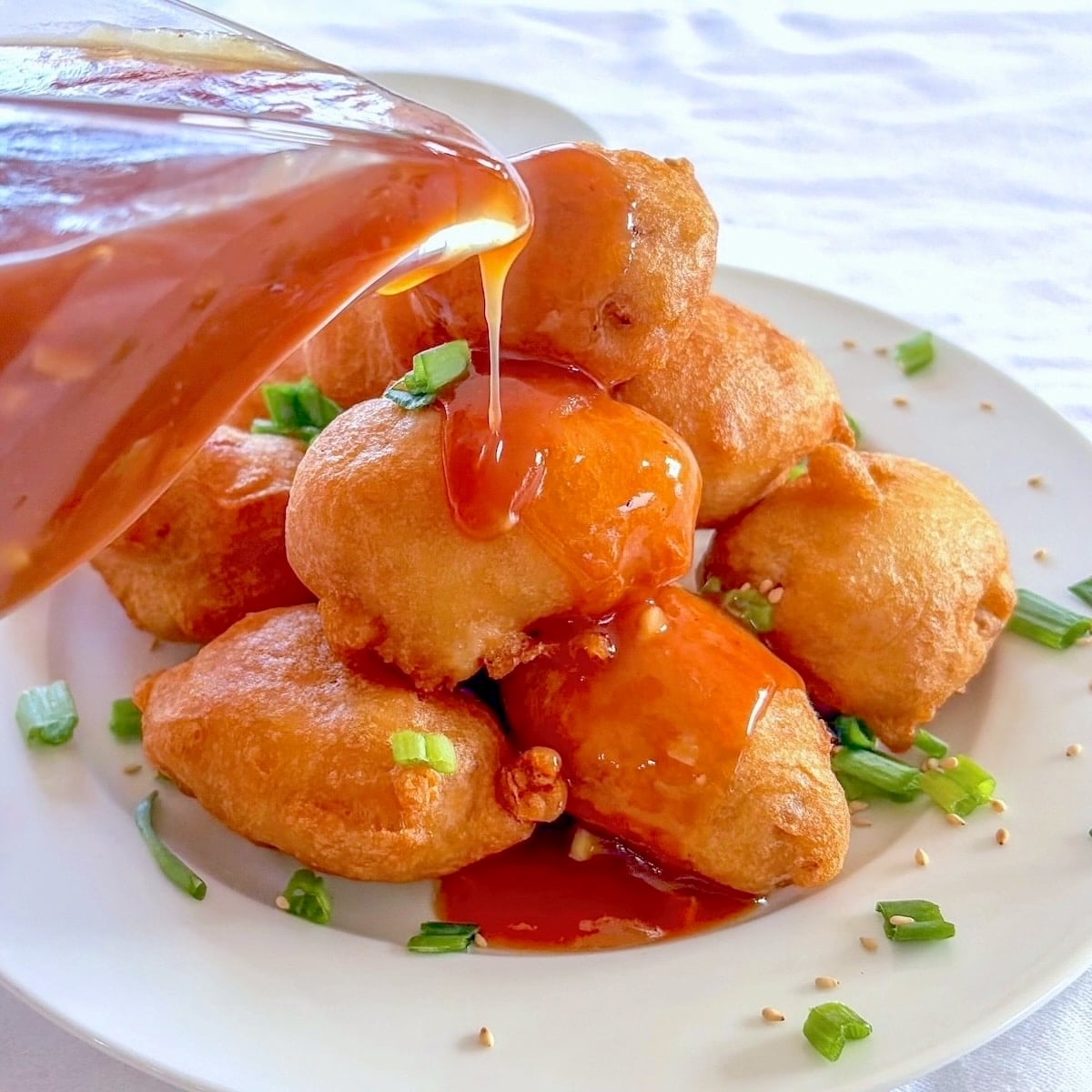 Chinese Chicken Balls photo with balls stacked on a plate with sweet and sour sauce being pored over the top.