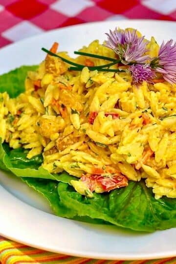 Creamy Curry Orzo Salad on a bed of lettuce on a white plate.