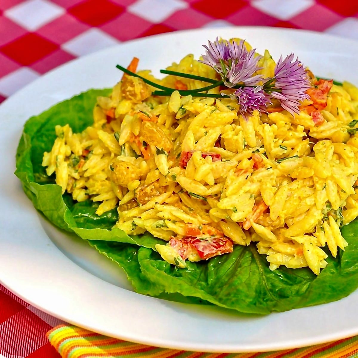 Creamy Curry Orzo Salad on a bed of lettuce on a white plate.