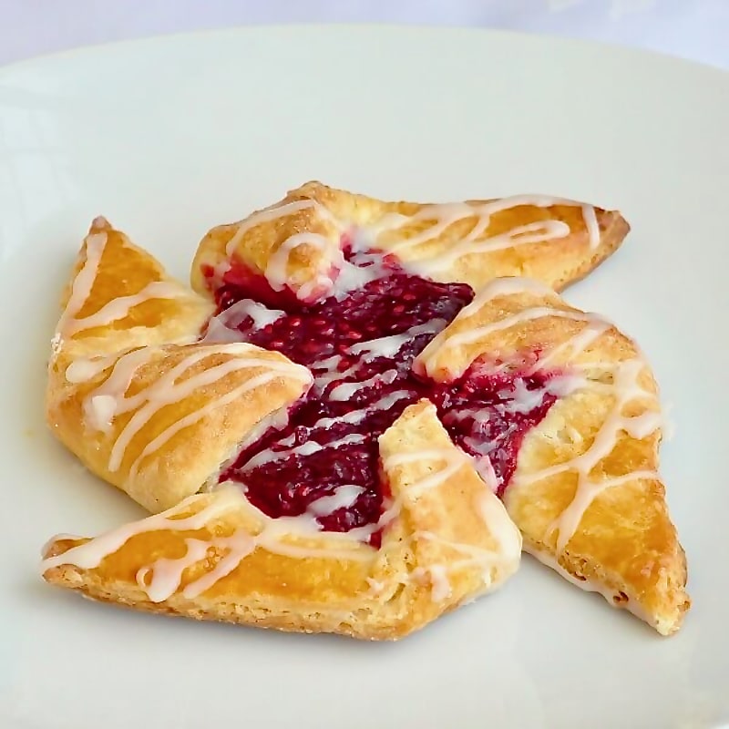 One raspberry pinwheel danish in a white plate.