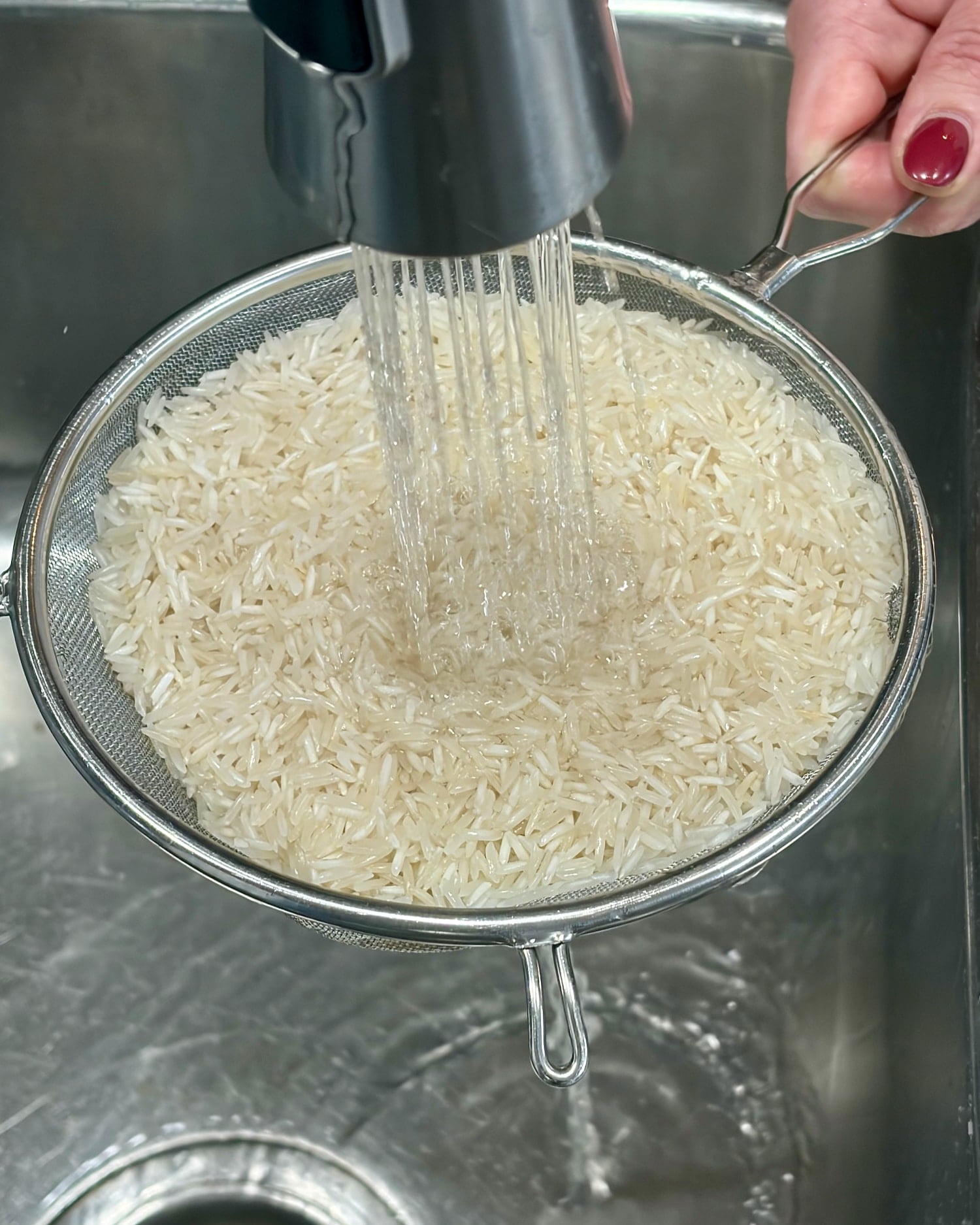 uncooked rice being rinsed under a running faucet