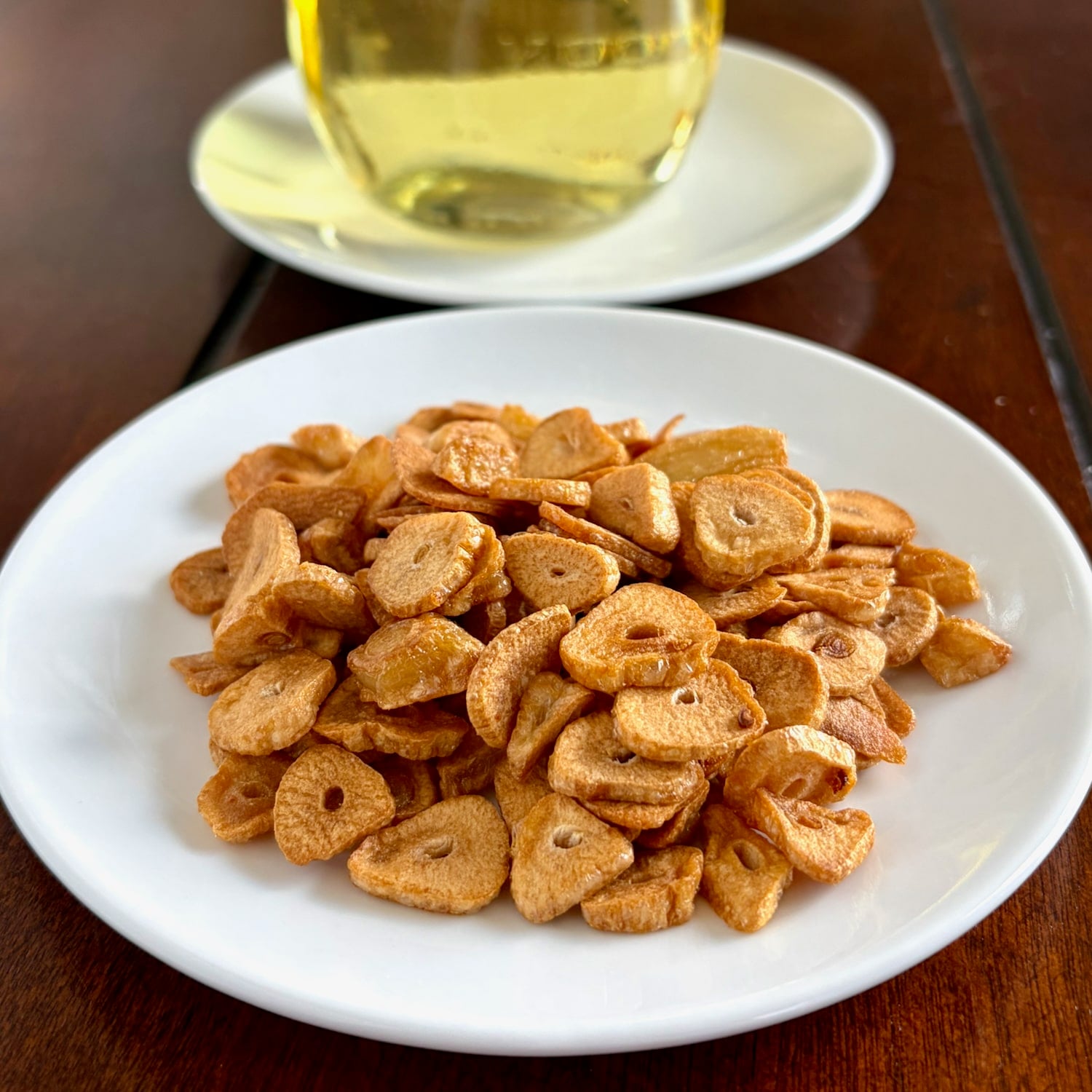 Crispy garlic on a white plate with garlic oil in background