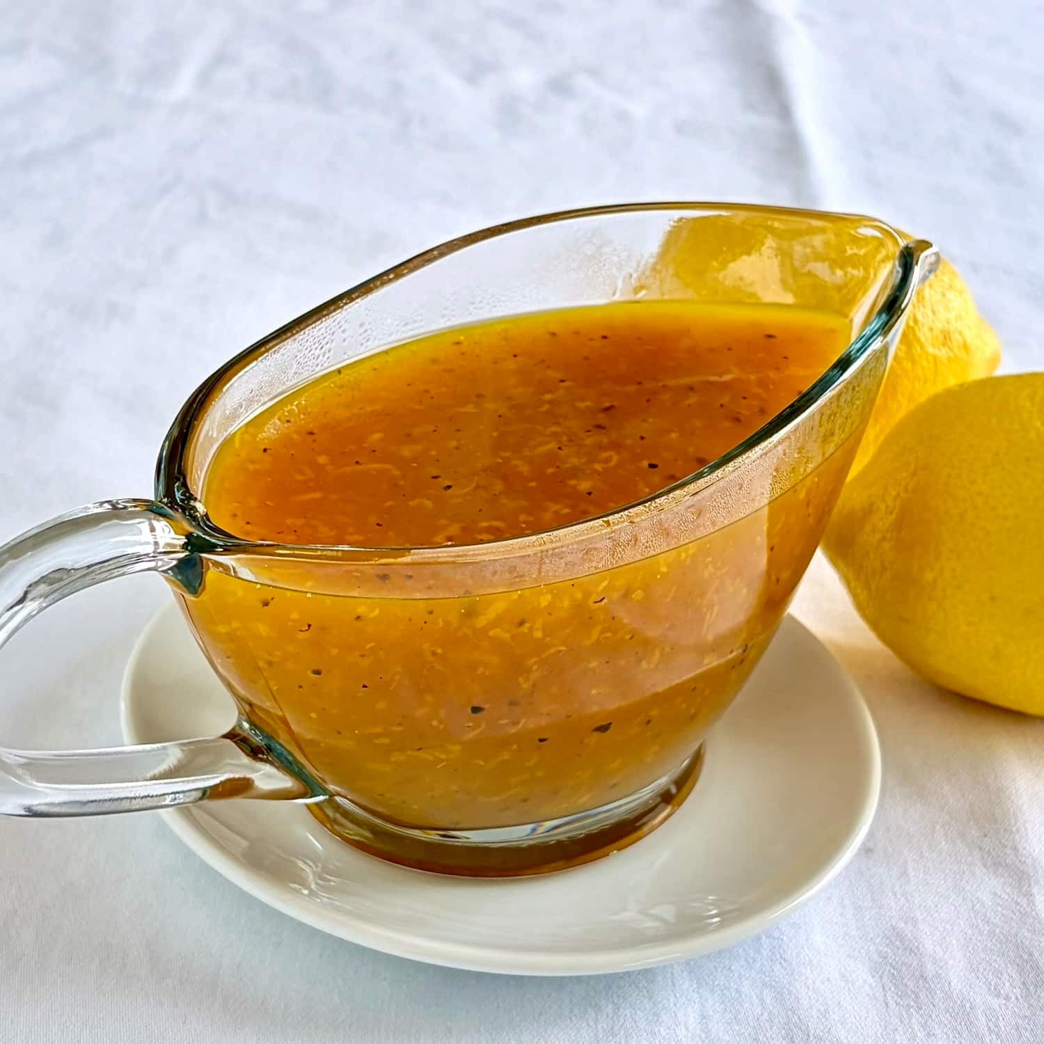 Photo of the best lemon sauce in a clear glass serving boat.