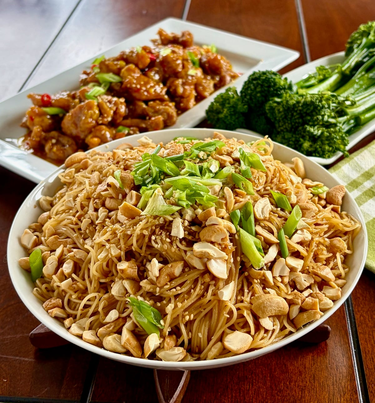 Sesame Garlic Noodles with Cashews in a serving bowl with asian chicken dish and broccolini in the background.