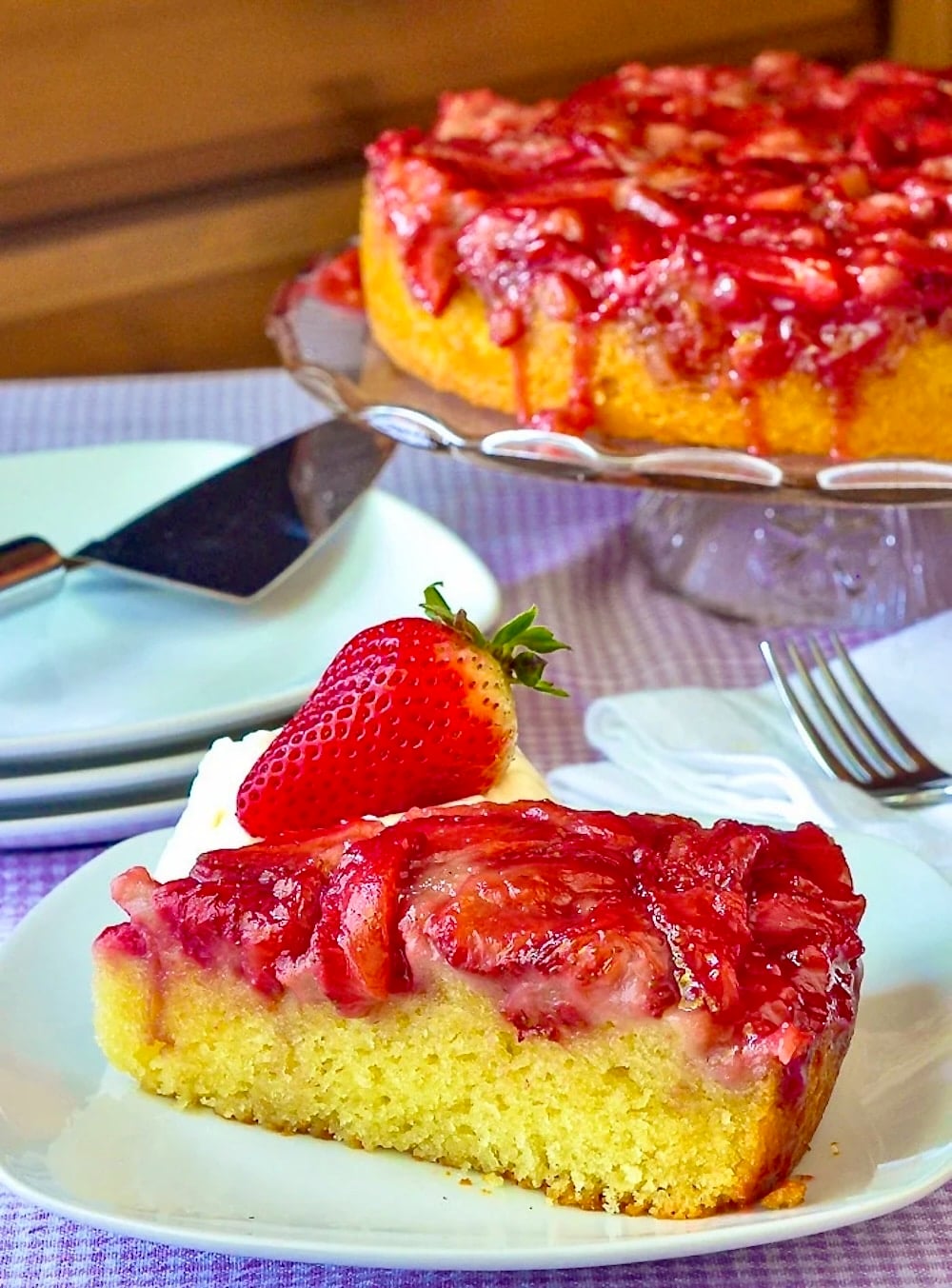 Strawberry Upside Down Cake photo of a slice of cake with whole cake on a pedestal in the background.