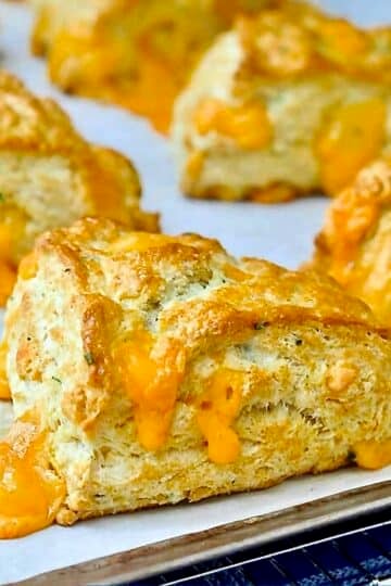 Cheddar Chive Buttermilk Biscuits resting on a parchment paper lined baking sheet.