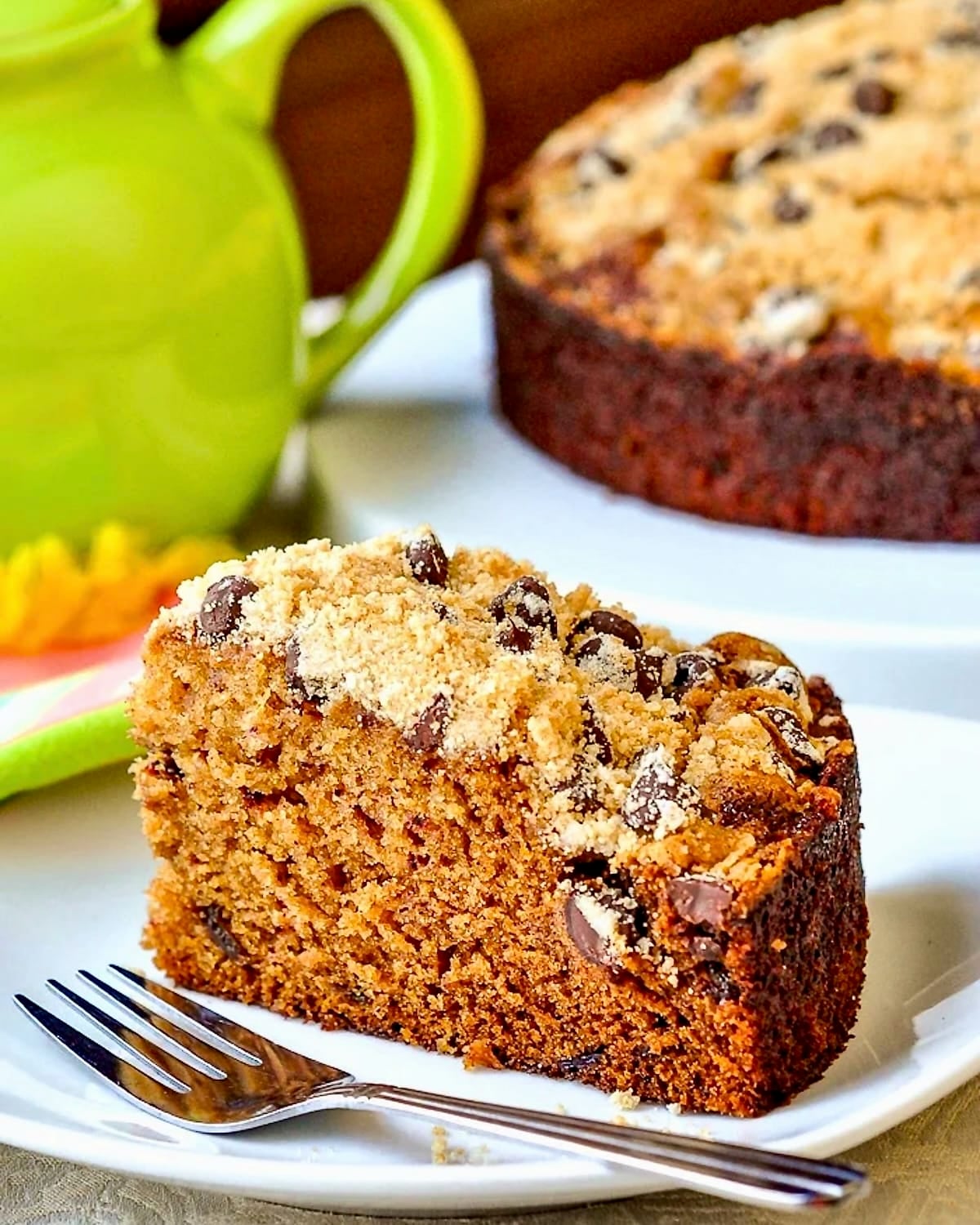 Date Coffee Cake with Chocolate Chip Streusel photo of single slice with whole cake in background.