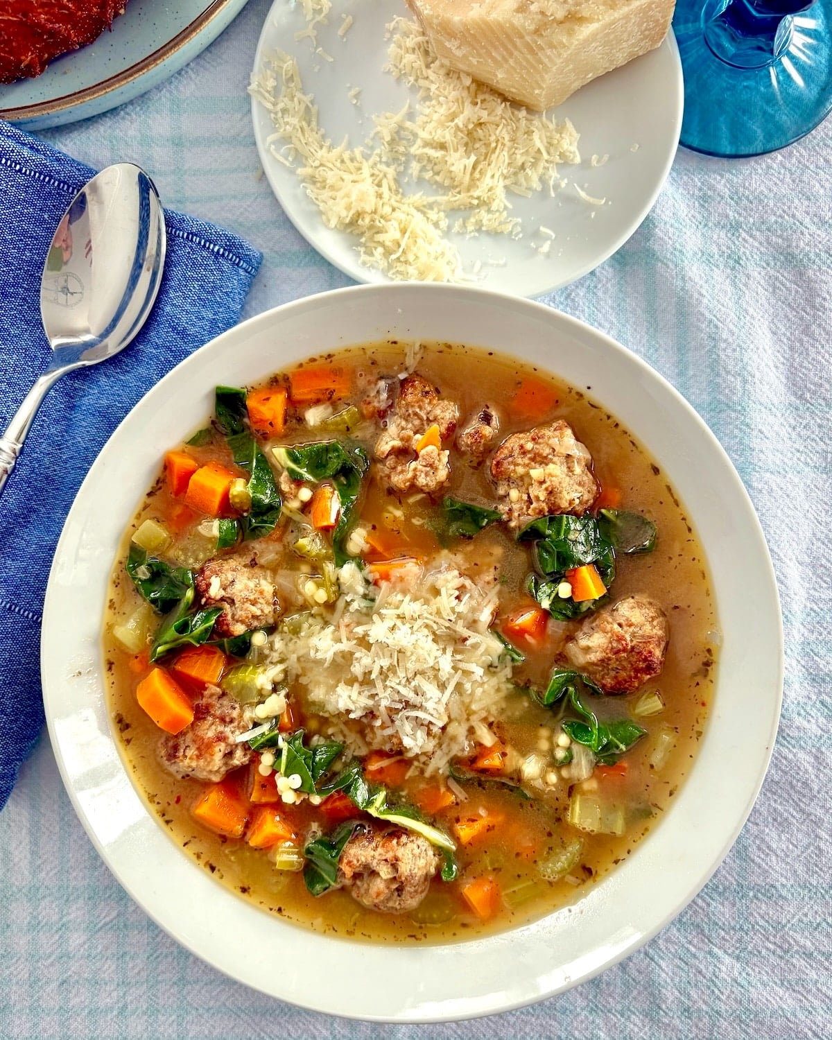 Overhead shot of one bowl of Italian wedding soup with grated Parmesan cheese next to it