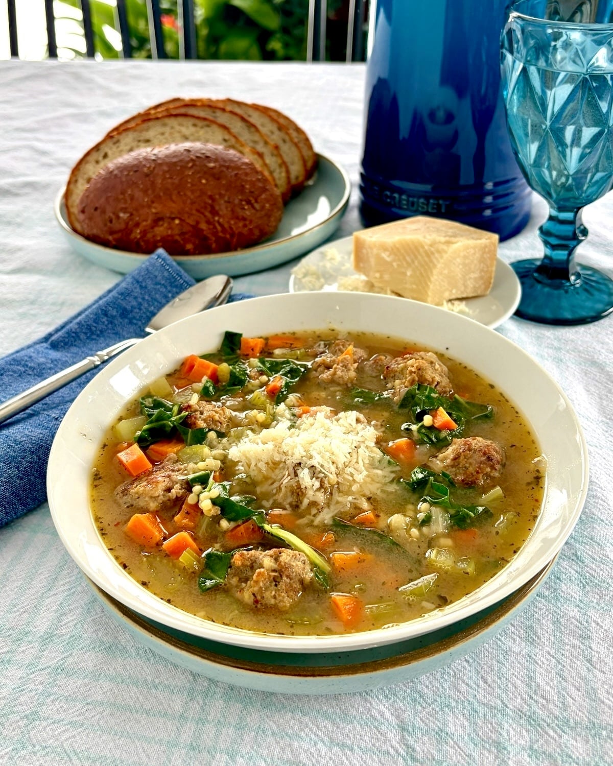 Photo of one bowl of Italian wedding soup with Parmesan cheese and bread in the background.