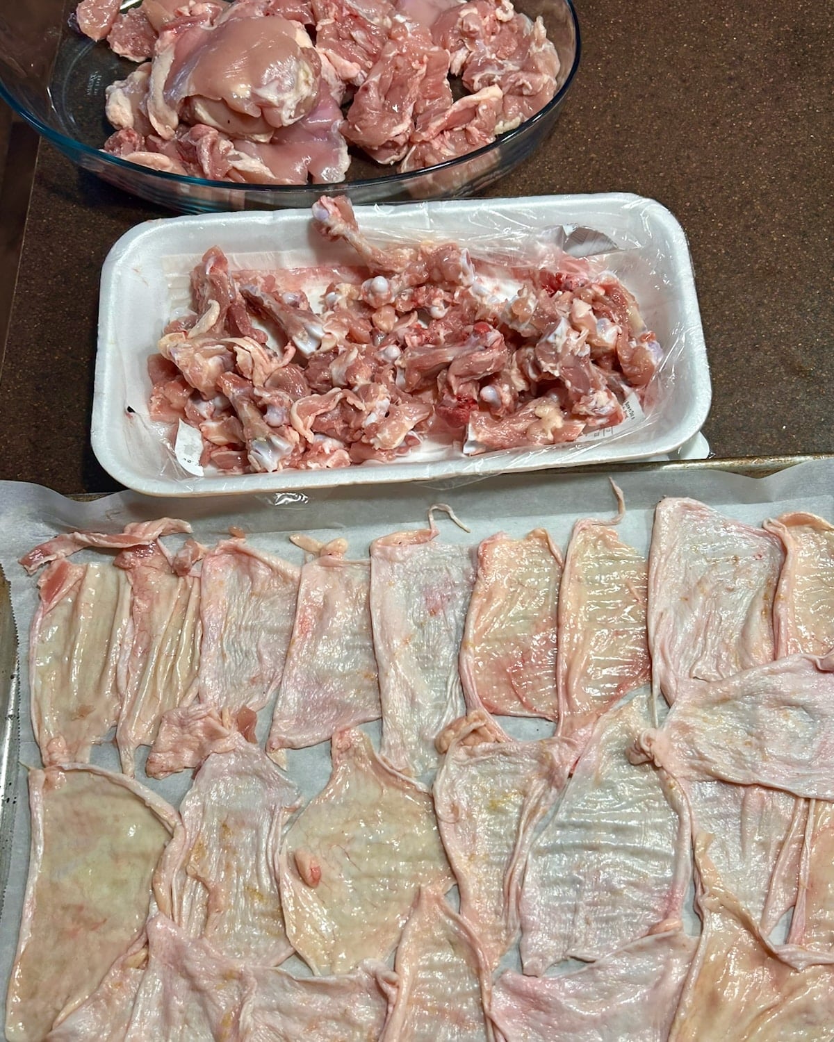 Chicken Thigh bones, boneless meat and chicken skins in a parchment lined sheet.