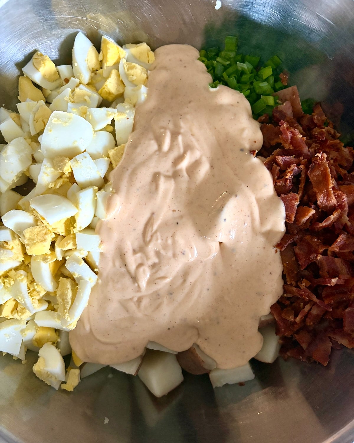 Ingredients for bacon and egg potato salad in a metal Bowl ready to be mixed together.