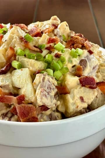 Close up photo of bacon and egg potato salad in a white bowl Square cropped for Google featured image.