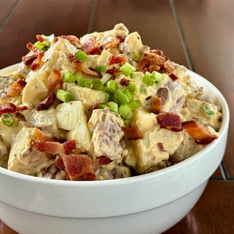 Close up photo of bacon and egg potato salad in a white bowl Square cropped for Google featured image.