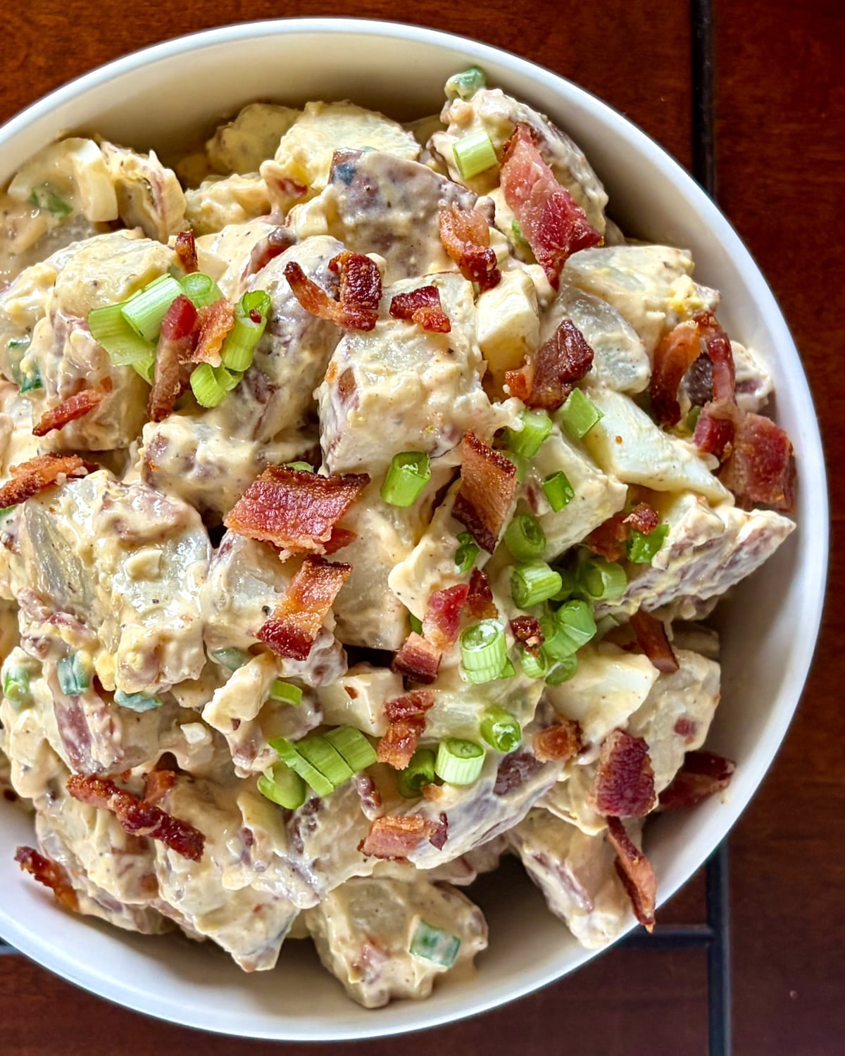 Overhead shot photo of bacon and egg potato salad with green onion and crumbled bacon garnishes on top.