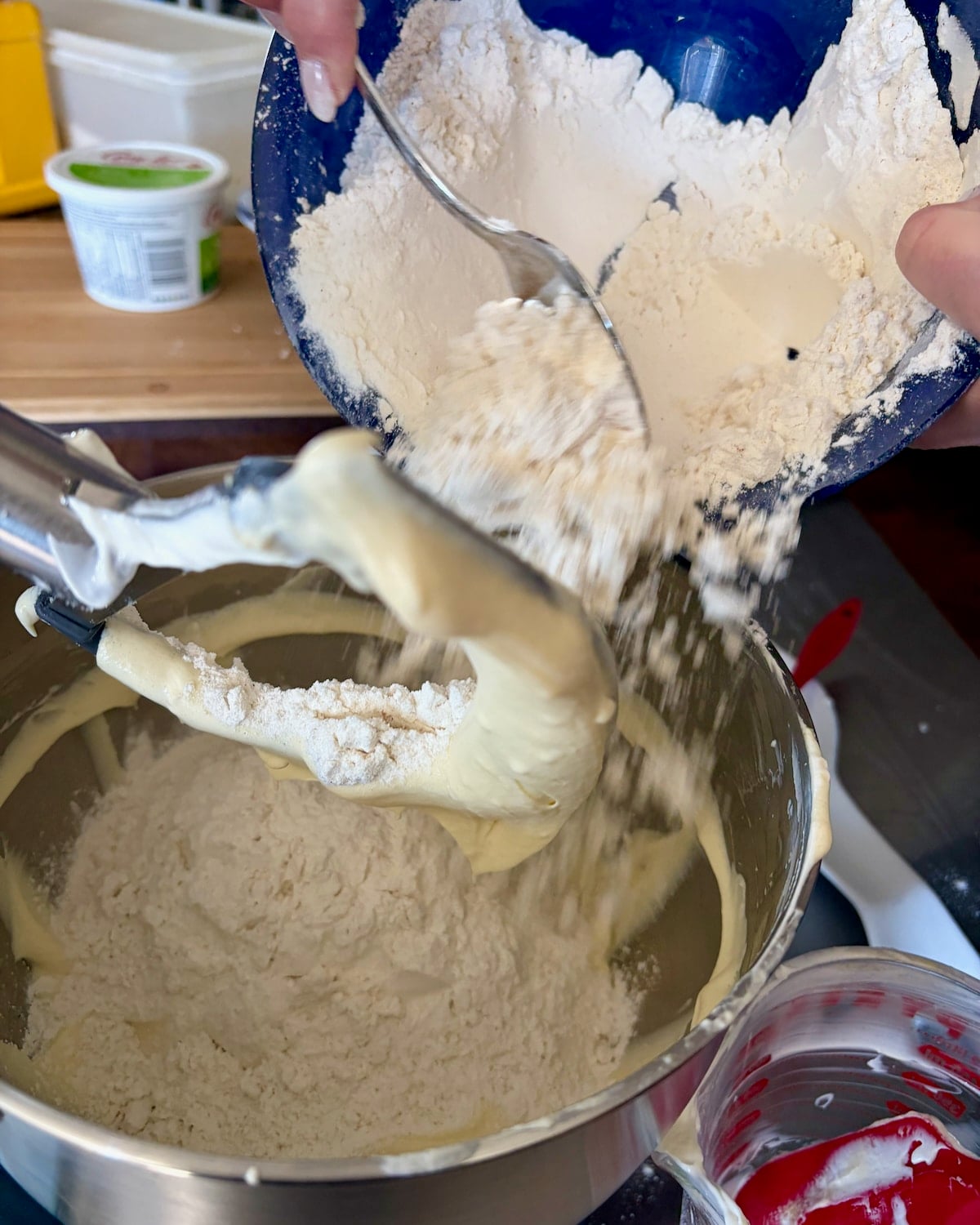 Photo of flower being added to a bowl to complete the dough for sour cream donuts.