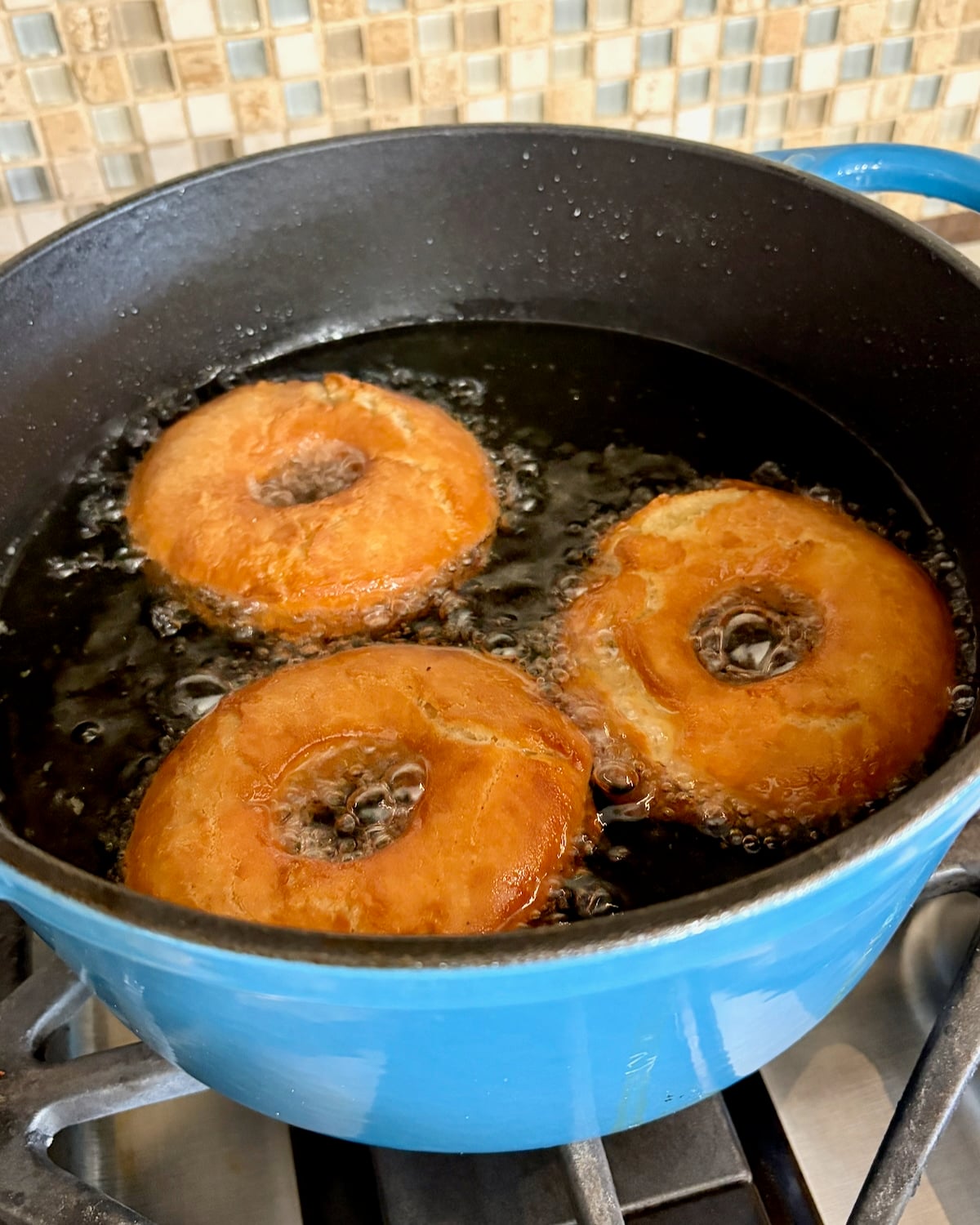 Photo of sour cream donuts being fried in a blue cast iron pot.