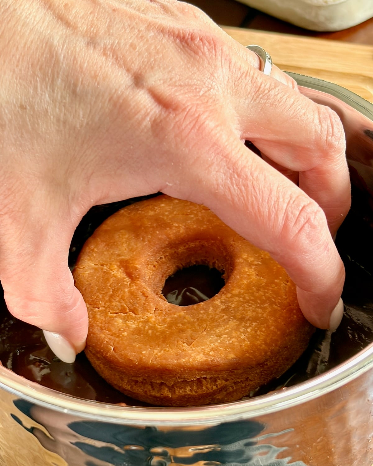 Photo of a hand dipping one sour cream donut into chocolate glaze
