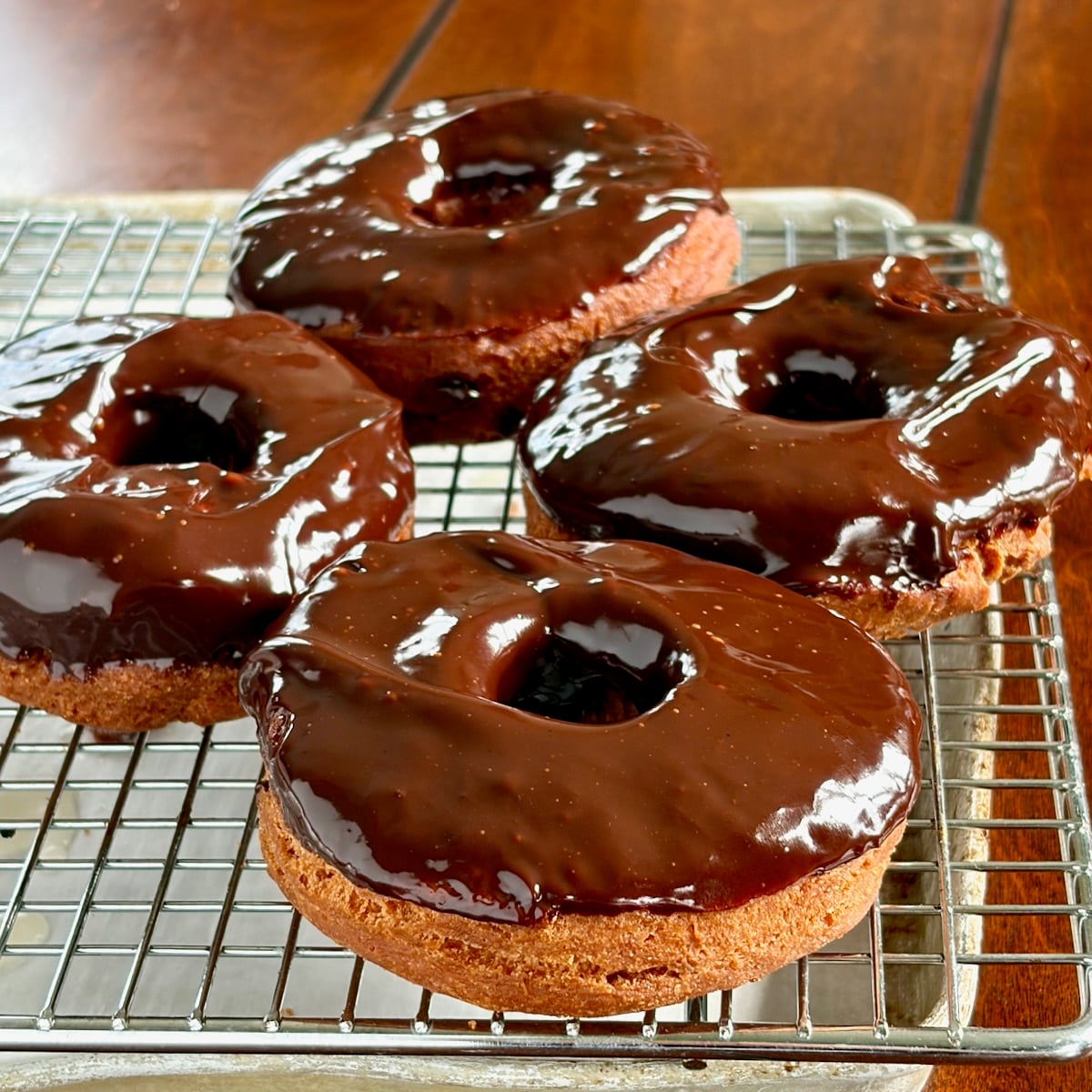 Close up photo of chocolate dipped sour cream donuts on a wire rack over a cookie sheet.