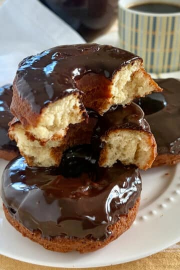 Photo of sour cream donuts stacked on a white plate with the Top Donut cracked in half to show interior crumb of the donut.