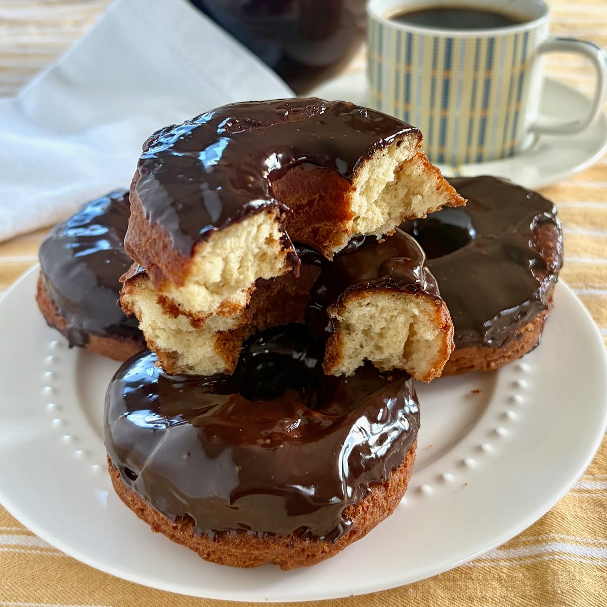 Photo of sour cream donuts stacked on a white plate with the Top Donut cracked in half to show interior crumb of the donut.