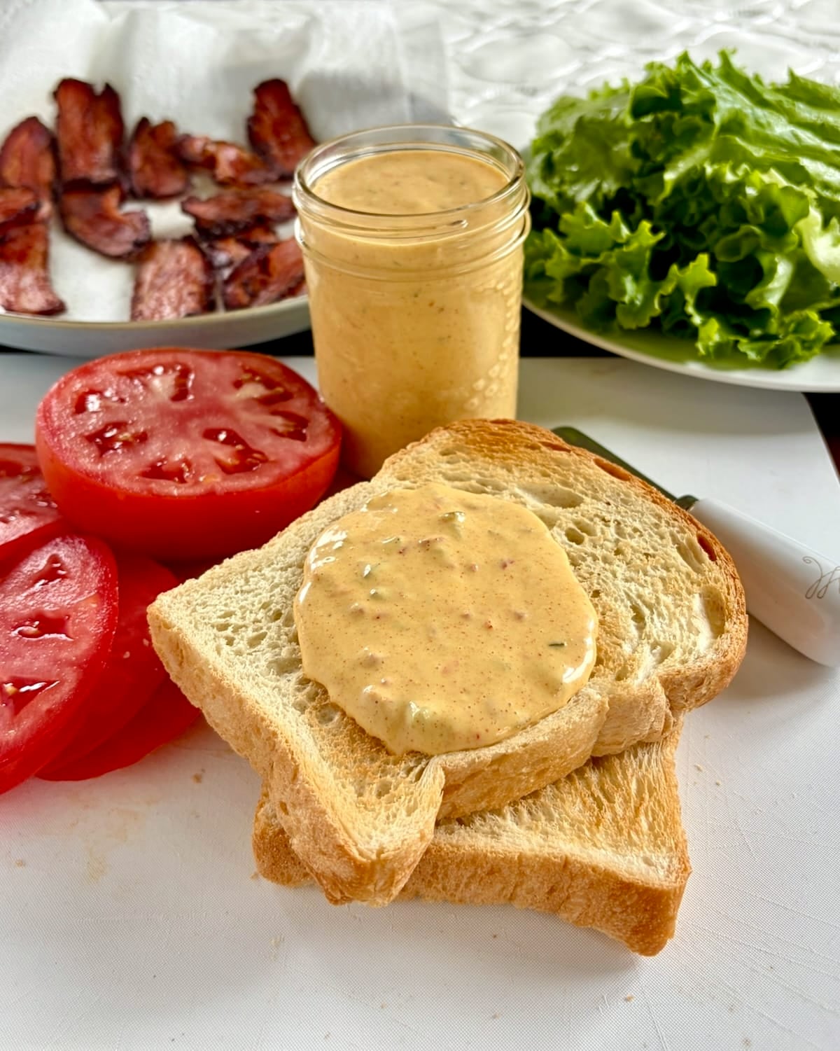 Photo of sandwich bread on toasted bread with bacon lettuce and tomato in the background
