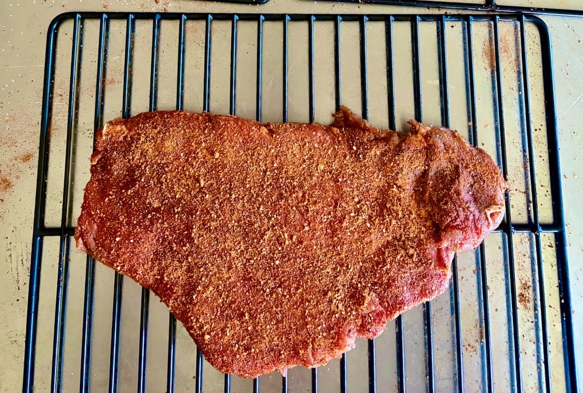 Photo of an uncooked rack of boneless ribs with seasoning rub added.