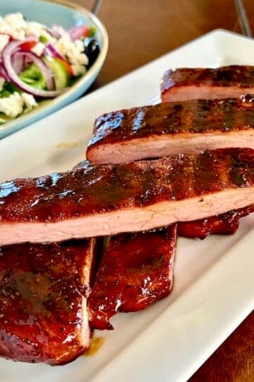 Barbecue Boneless Ribs sliced and stacked n a white serving platter, square cropped photo for Google Featured image