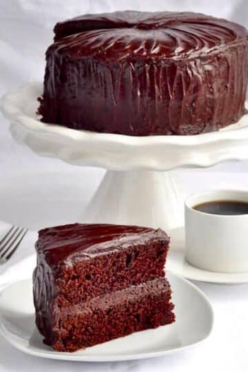 Chocolate Fudge Cake with Easy Fudge Frosting photo of one slice with whole cake in pedestal in the background