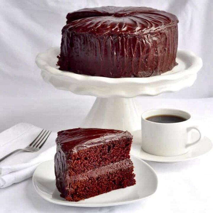 Chocolate Fudge Cake with Easy Fudge Frosting photo of one slice with whole cake in pedestal in the background