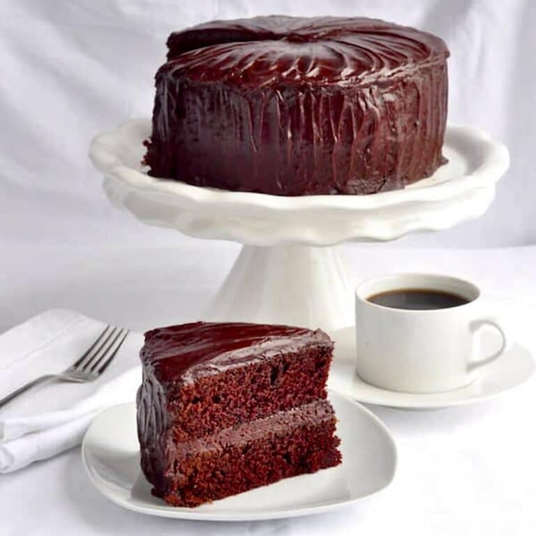 Chocolate Fudge Cake with Easy Fudge Frosting photo of one slice with whole cake in pedestal in the background
