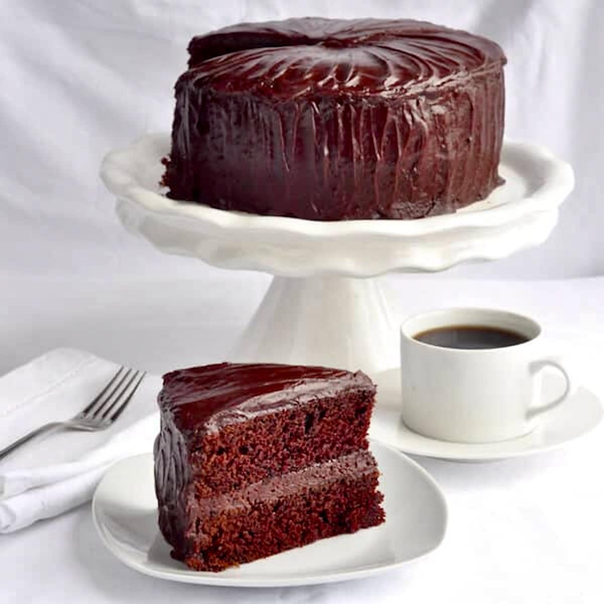 Chocolate Fudge Cake with Easy Fudge Frosting photo of one slice with whole cake in pedestal in the background