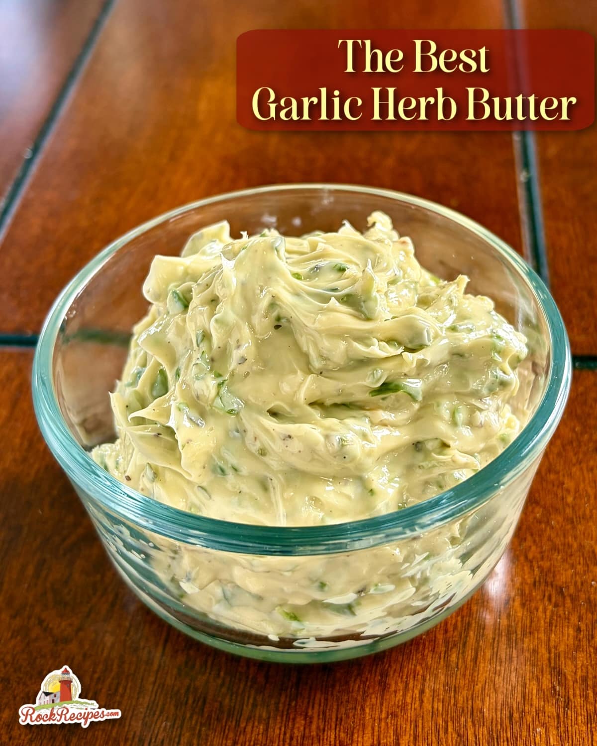 Close up photo of soft, spreadable Garlic Herb Butter in a clear glass serving bowl with title text added for social media posts and Pinterest.