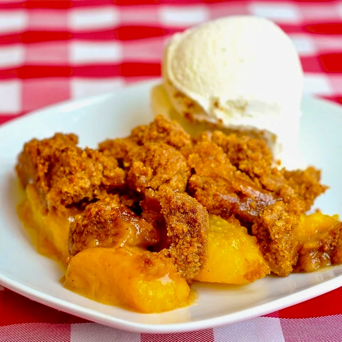 Ginger Snap Peach Crumble photo of a single serving on a white plate with vanilla ice cream.