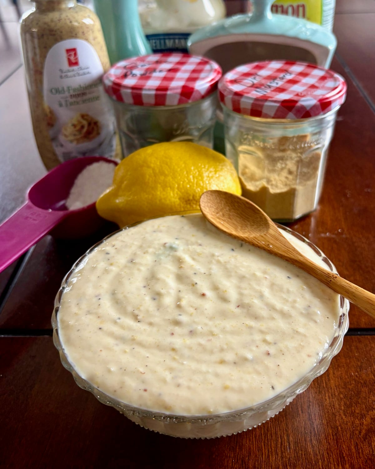 Photo of a wooden spooon sitting atop a small bowl of Creamy Lemon Parmesan Salad Dressing