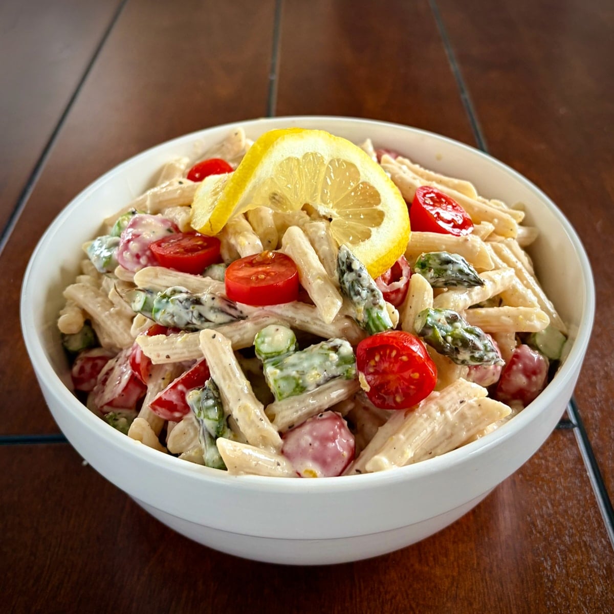 Wide shot of a bowl of Lemon Parmesan Pasta Salad on a dark wooden table.