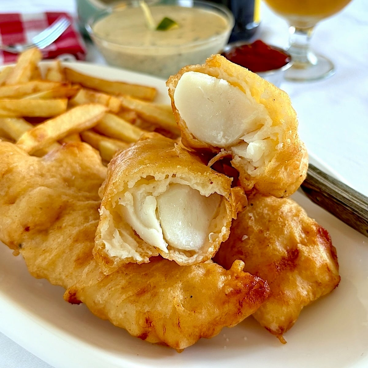 Super Crispy fish and chips close up photo of one piece of cooked fish broken open to reveal interior.